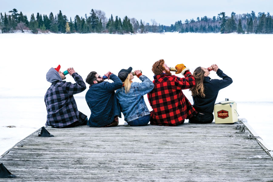 Group of adults drinking cans of beer on dock