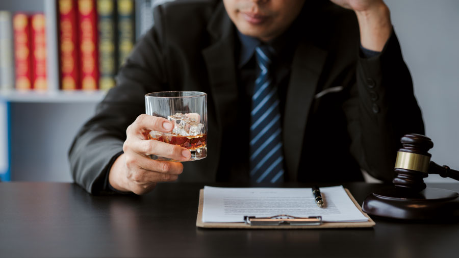 Man at desk holding glass of alcohol