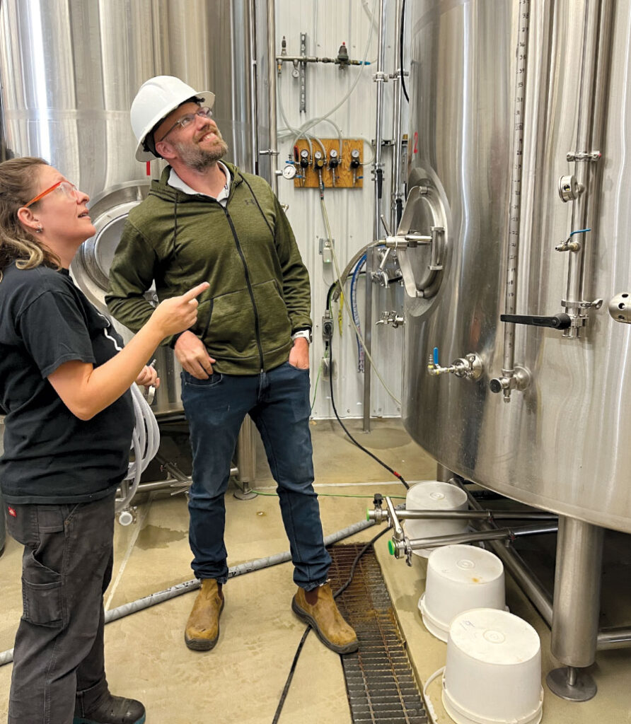 Man and woman smiling, looking at brewing equipment