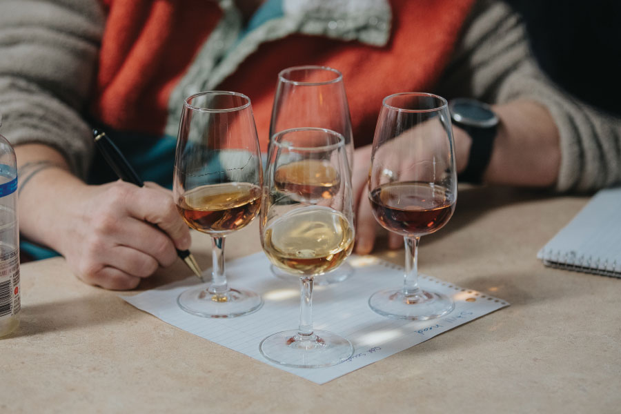 woman writing on paper with four glasses of spirits on table