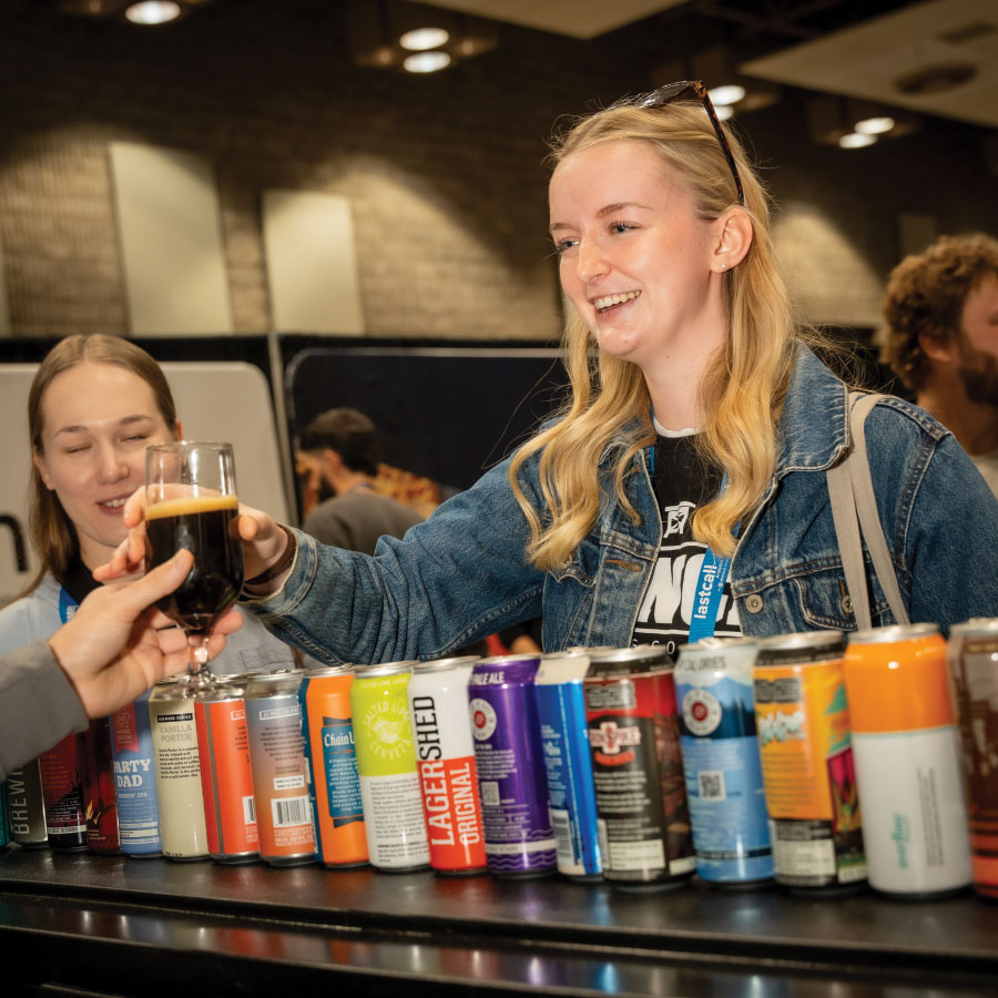 Attendee smiling reaching for glass of dark beer with row of colourful cans on counter