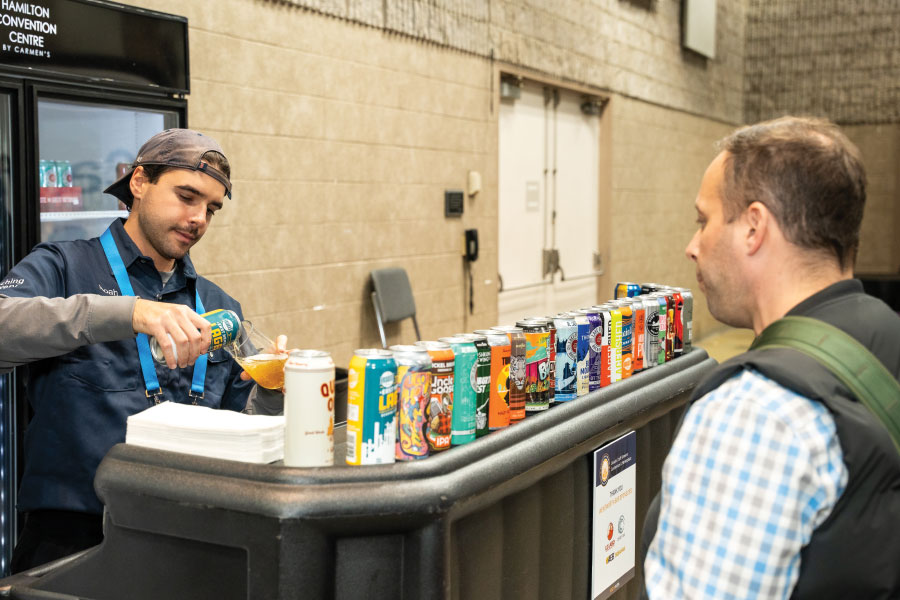 Attendee watching beer being poured into glass with row of colourful cans on counter