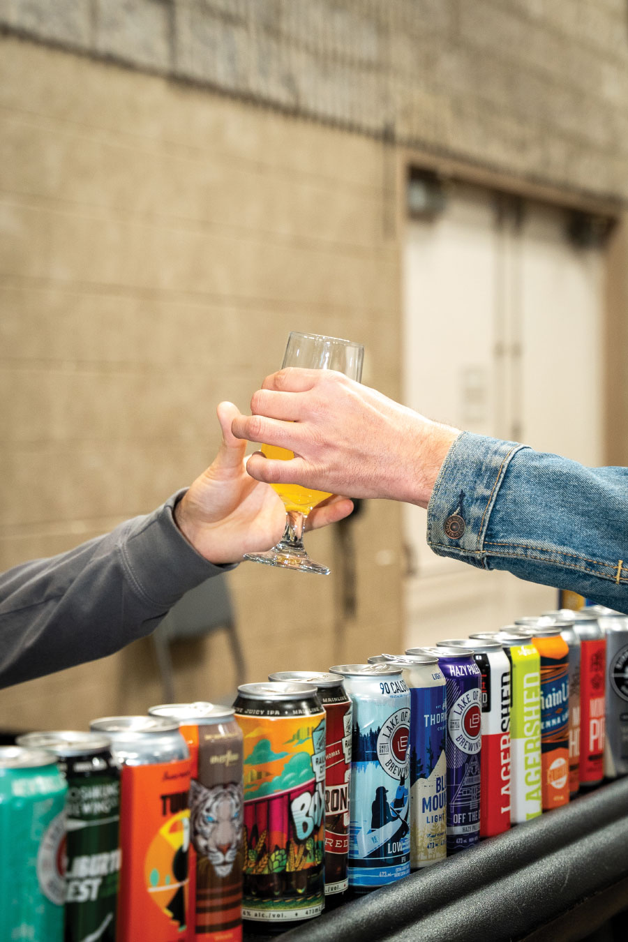 Attendee reaching for glass of beer with row of colourful cans on counter