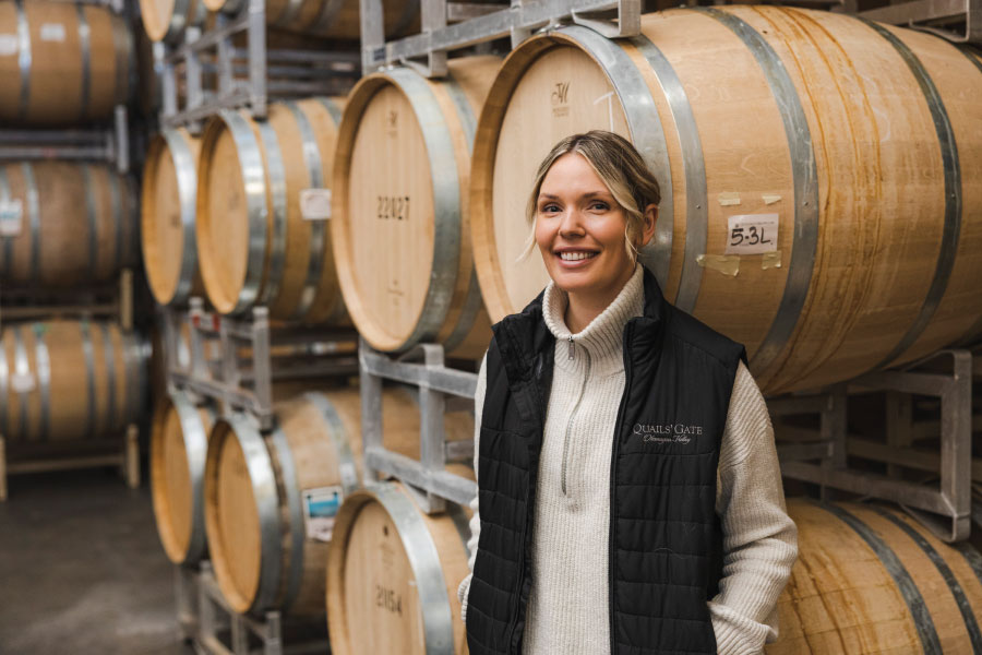 Kailee standing in front of rows of wooden wine barrels