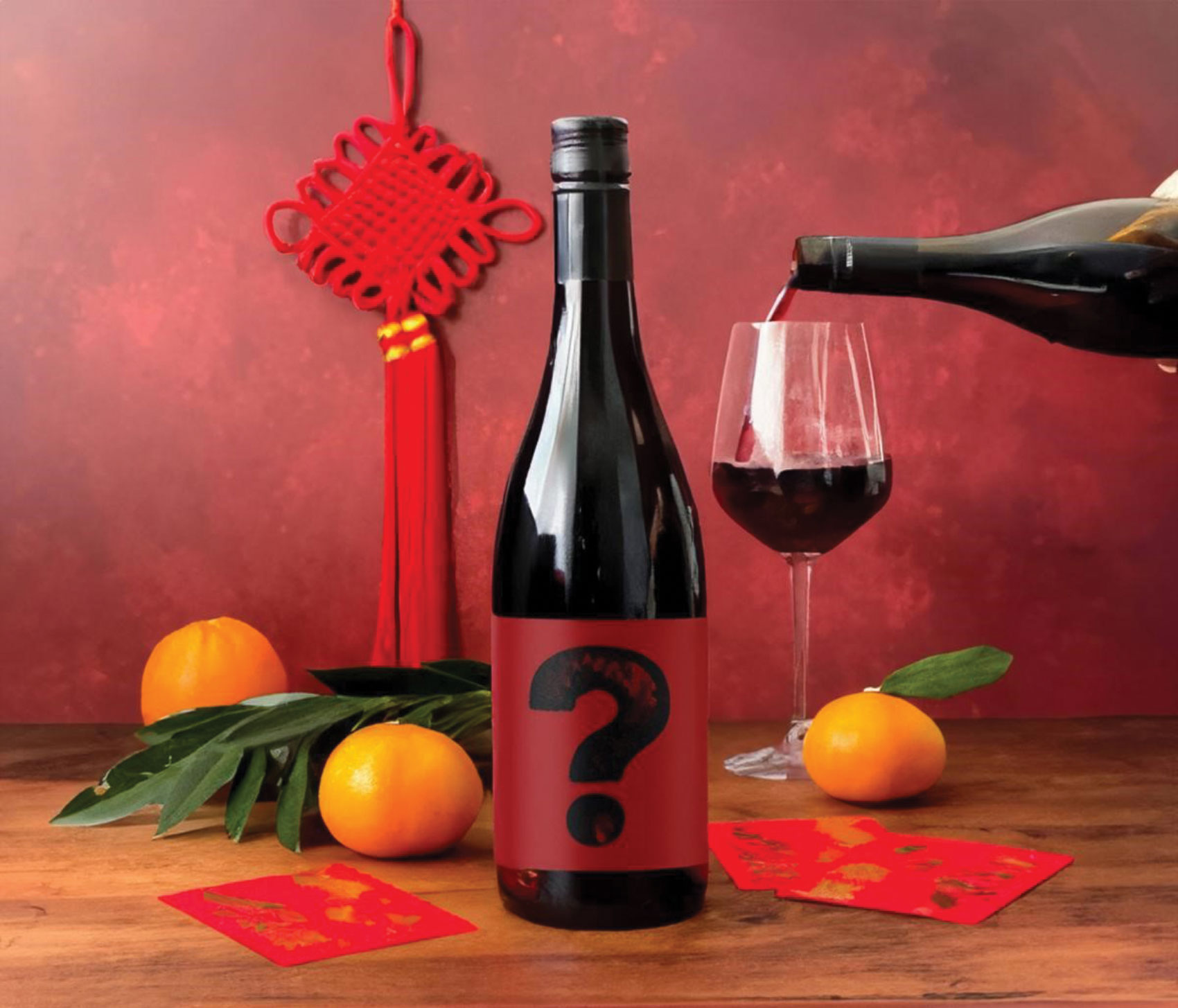 Bottle of red wine with question mark on label on table alogn with fruit and a glass of wine being poured from another bottle