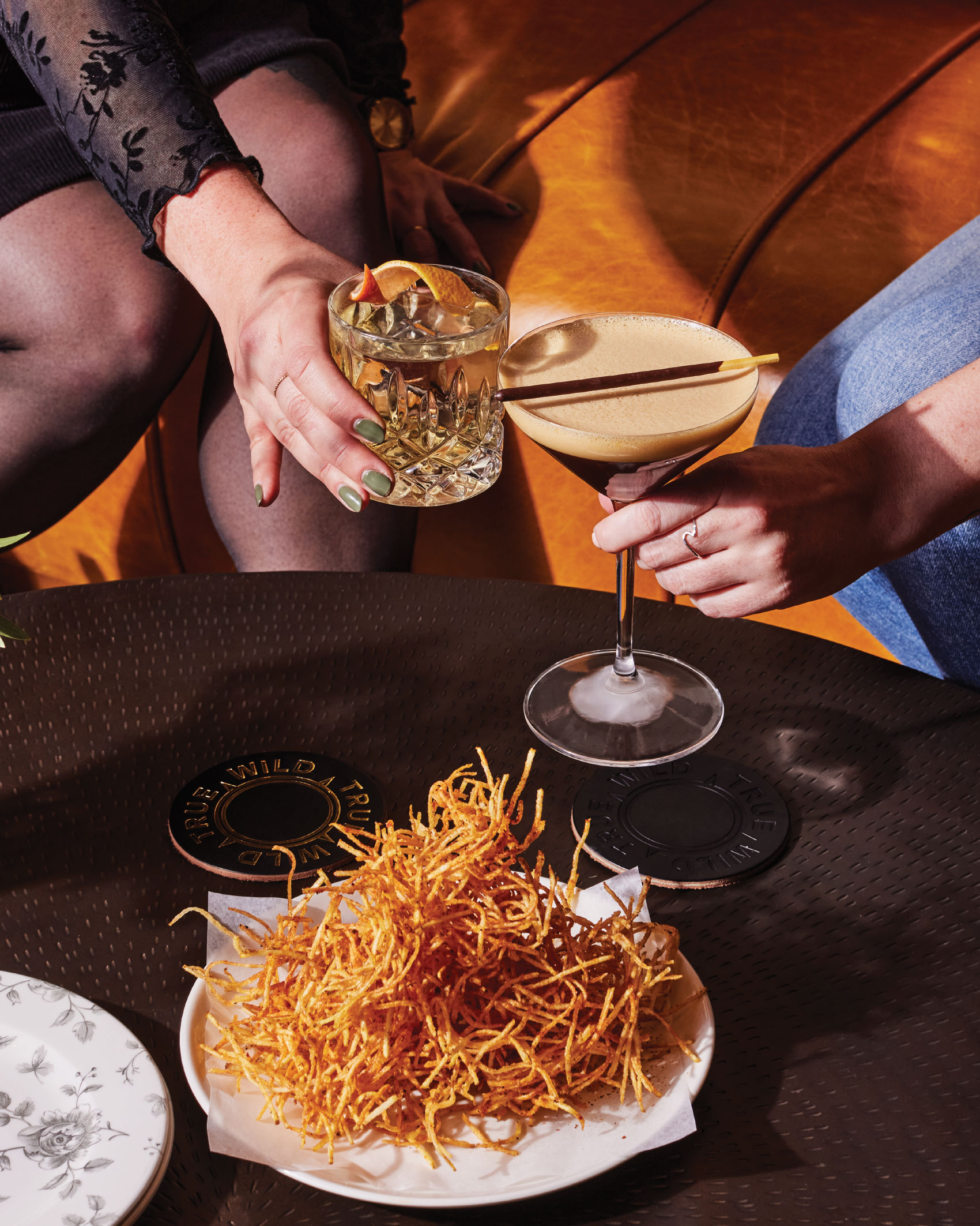 Couple toasts cocktails at table with plate of food